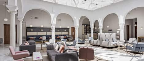 A spacious lobby with modern seating, a bar area, and a high ceiling with geometric patterns.