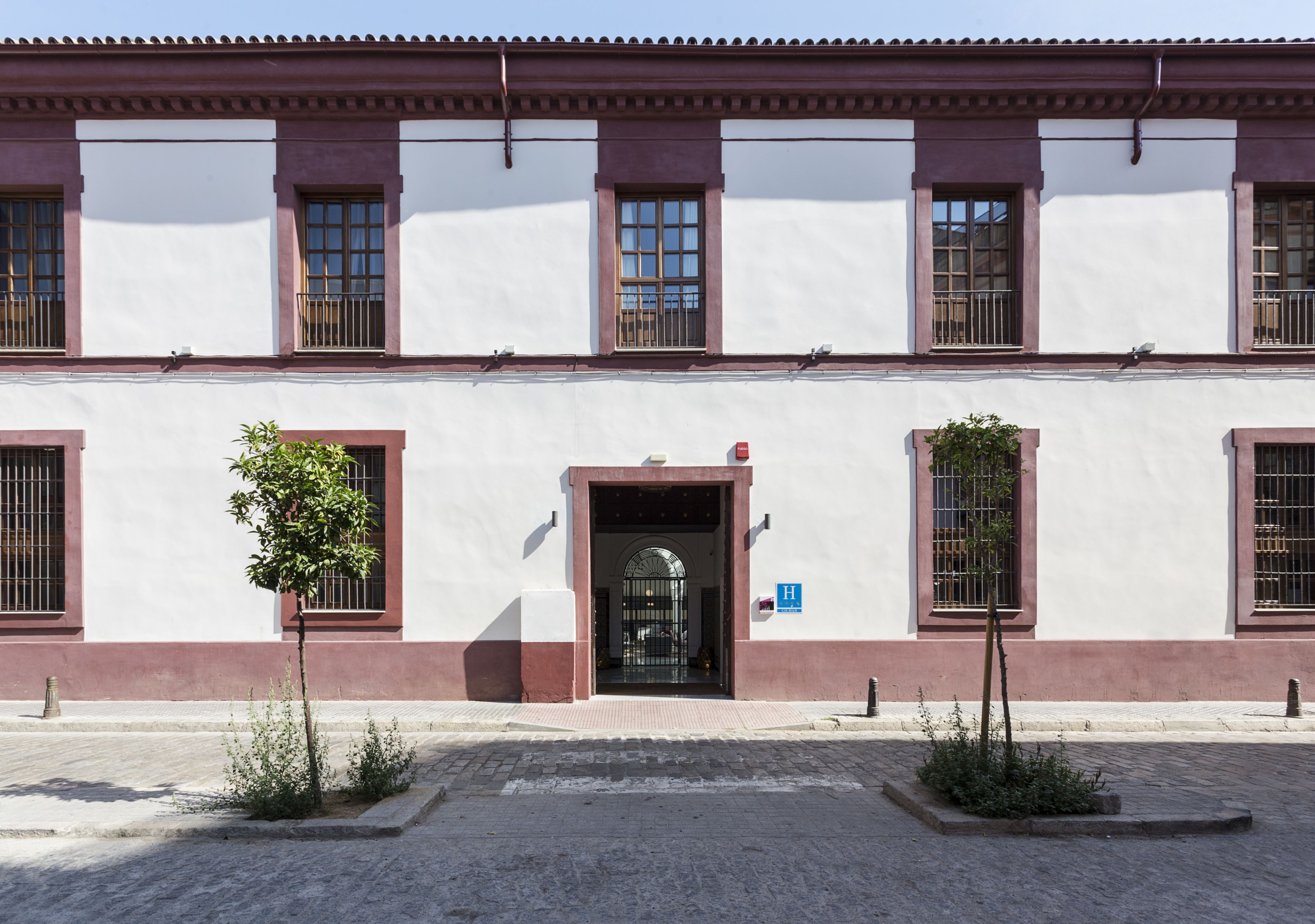 A building with a white facade and red trim, featuring a central entrance with a black door and a blue sign indicating a hospital.