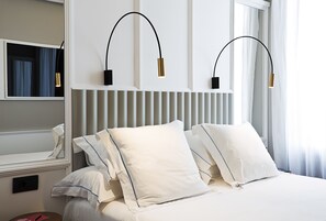 Hotellihuone, jossa on suuri sänky, valkoiset vuodevaatteet ja kaksi seinälle asennettua lamppua.