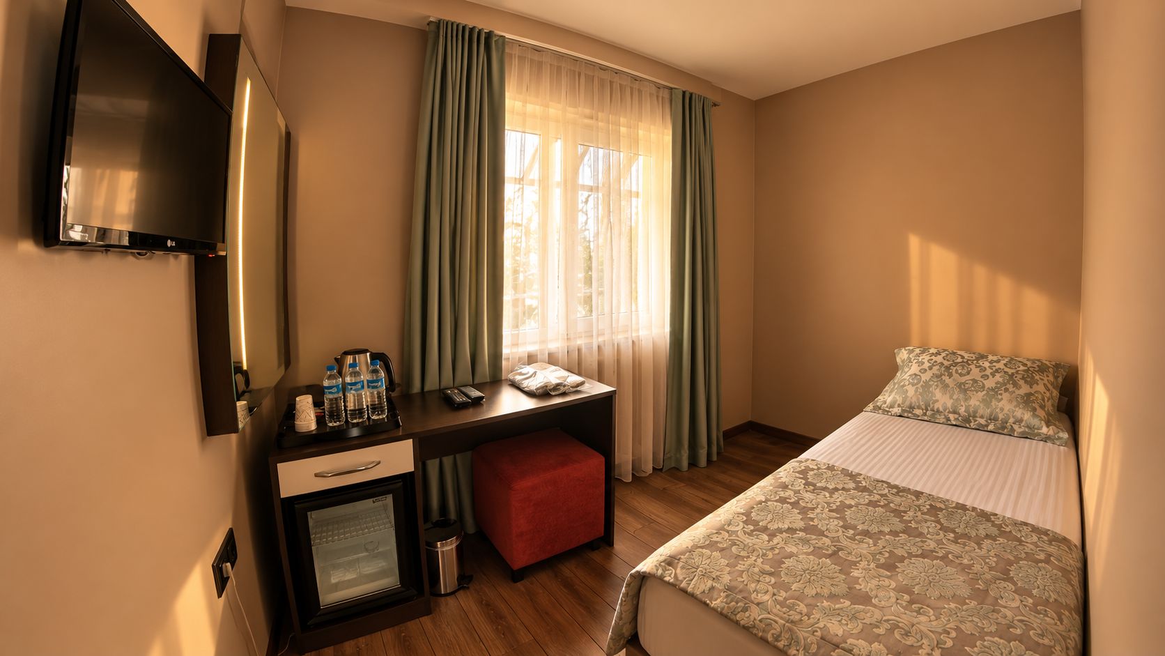 Une chambre d’hôtel avec un lit, un bureau doté d’un mini-réfrigérateur, une télévision et une fenêtre avec des rideaux.