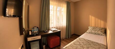 Une chambre d’hôtel avec un lit, un bureau doté d’un mini-réfrigérateur, une télévision et une fenêtre avec des rideaux.