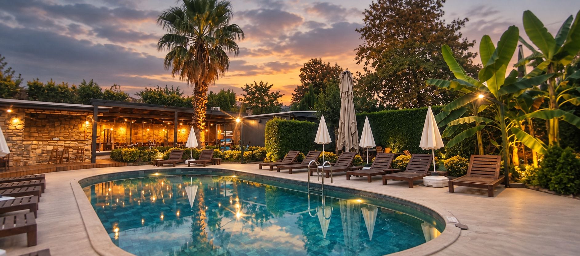 Piscina com espreguiçadeiras e guarda-sóis, cercada por vegetação e uma parede de pedra.