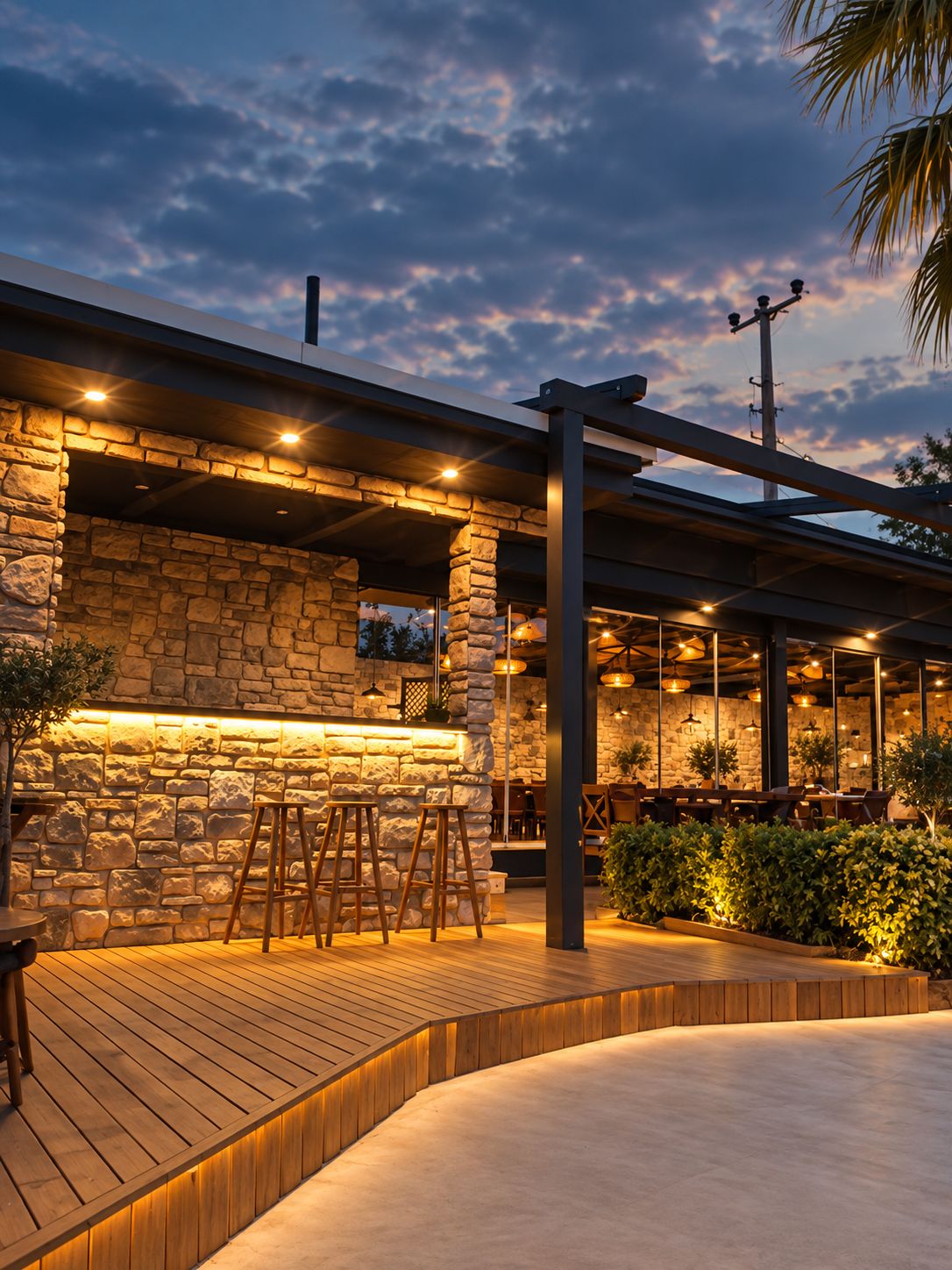 An outdoor seating area with stone walls, wooden flooring, and overhead lighting.