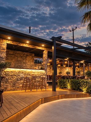 An outdoor seating area with stone walls, wooden flooring, and overhead lighting.