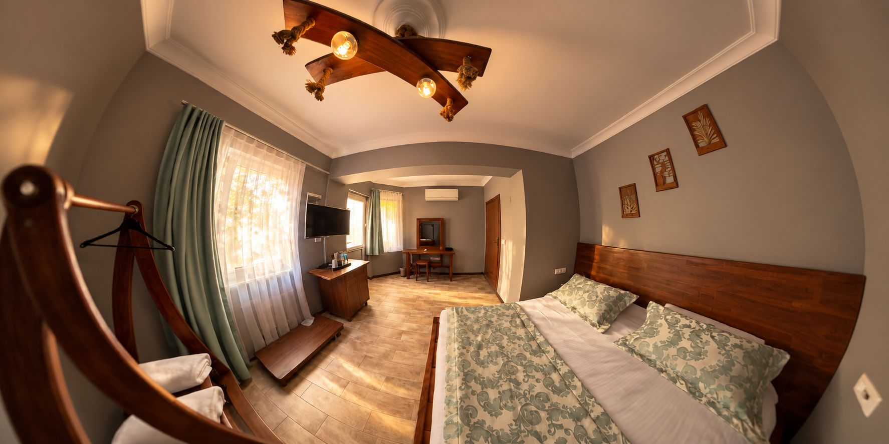 A hotel room with a bed, a wooden headboard, a desk with a chair, a television, and a window with curtains.