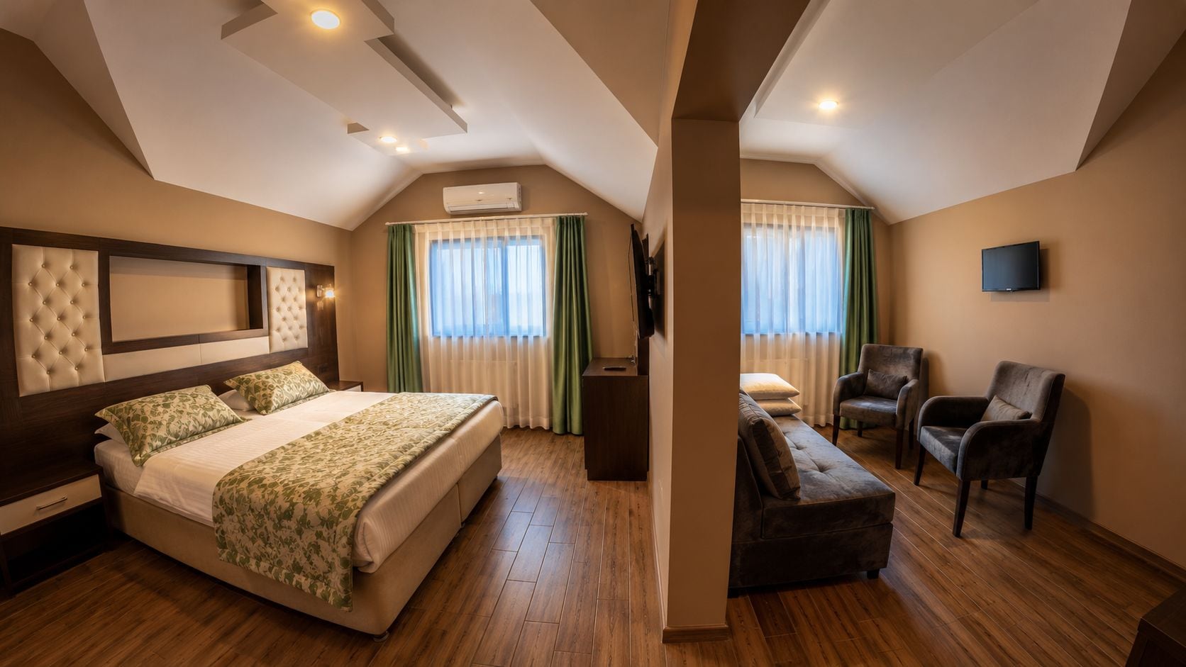 A hotel room with a large bed, a sofa, a chair, and a TV.