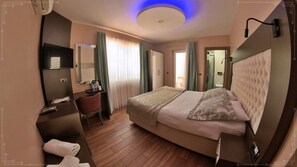 Une chambre d’hôtel équipée d’un lit, d’un bureau, d’une chaise, d’un miroir, d’une télévision et d’une salle de bain.