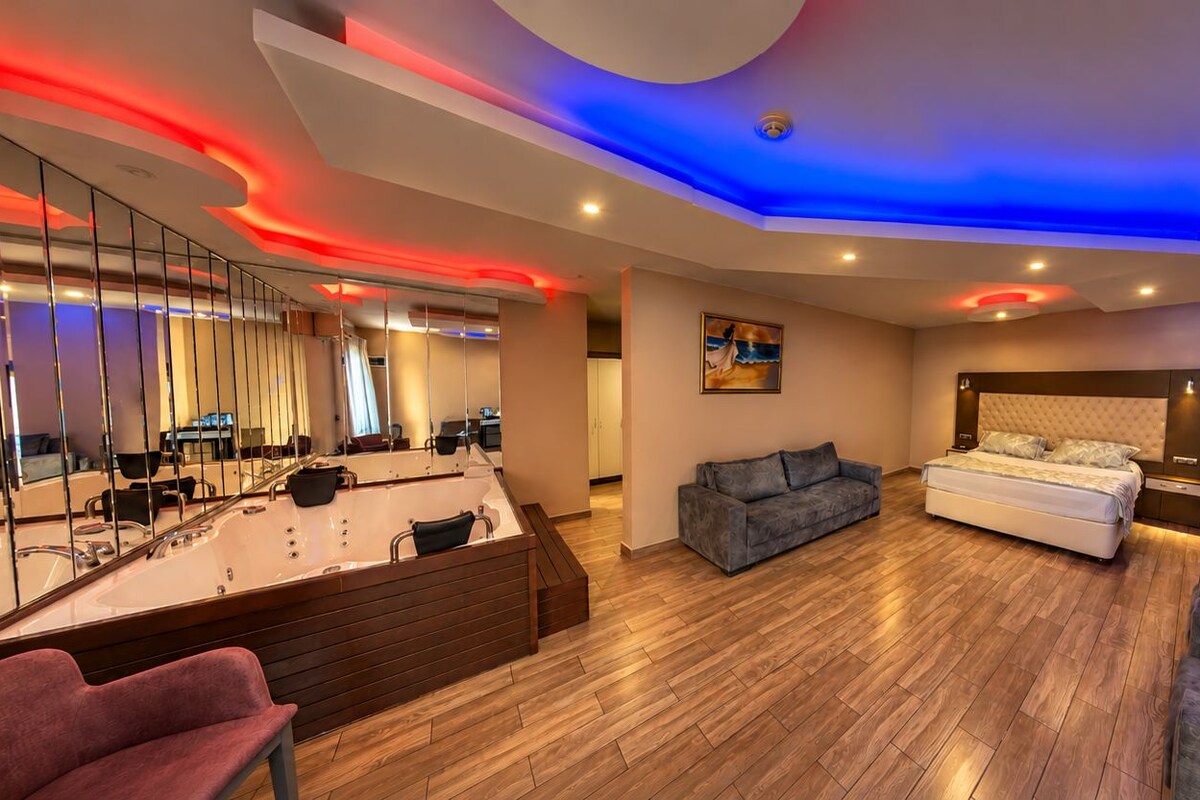 A modern bedroom with a large bed, a sofa, a TV, and a bathroom with a mirror and sink.