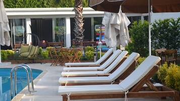 Un área junto a la piscina con sillones de descanso, una palmera y mobiliario exterior.
