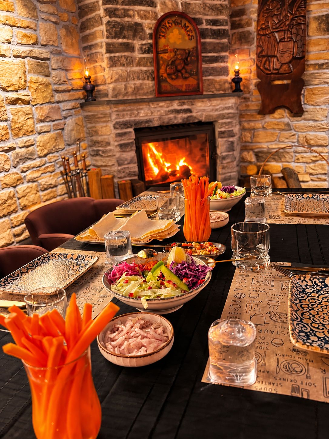 A dining table set with plates, bowls, and glasses, a fireplace, and stone walls.