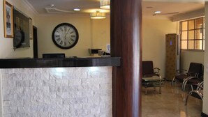 A reception area with a marble counter, a large wall clock, and a seating area with chairs. - Beni Apartment And Suites (Lagos)