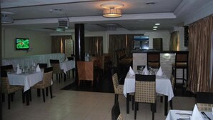 A restaurant with multiple dining tables, chairs, and a television screen on the wall. - Beni Apartment And Suites (Lagos)