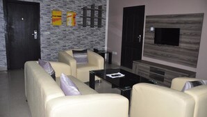 A living room with a sofa set, a coffee table, and a flat-screen TV mounted on the wall. - Beni Apartment And Suites (Lagos)
