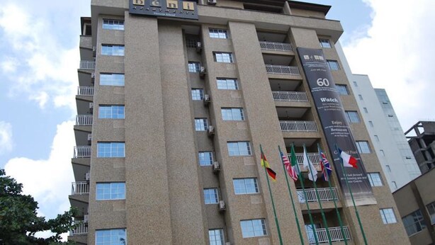 A multi-story hotel building with balconies, a prominent sign indicating 60 rooms, and multiple flags displayed outside. - Beni Apartment And Suites (Lagos)