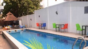 A swimming pool with a tiled edge, surrounded by a white wall. There are chairs and tables with colorful cushions outside the pool area. - Beni Apartment And Suites (Lagos)