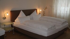Una cama bien hecha con sábanas blancas, una mesita de noche con lámpara y una lámpara de pared.