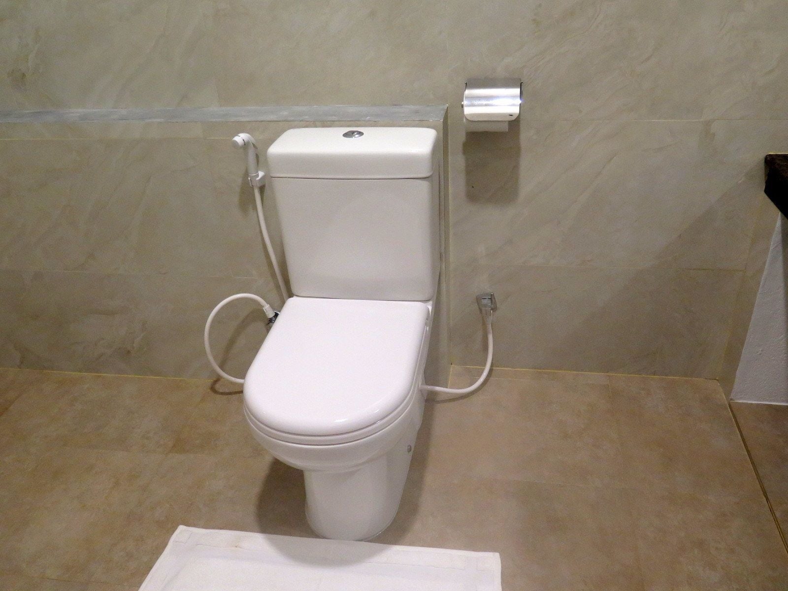 A standard white toilet with a flush handle and a paper towel dispenser on the wall.