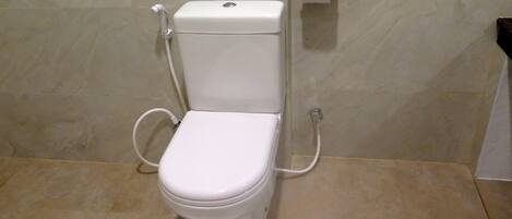A standard white toilet with a flush handle and a paper towel dispenser on the wall.
