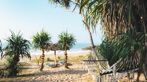 A sandy beach with palm trees, a hammock, and lounge chairs. - Ananya Beach Resort (Rekawa)