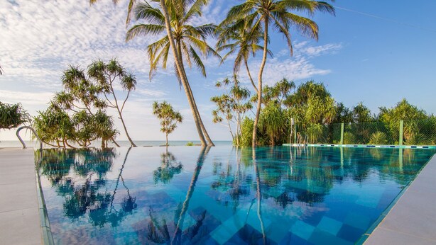 An infinity pool with clear blue water reflecting palm trees and a clear sky. - Ananya Beach Resort (Rekawa)