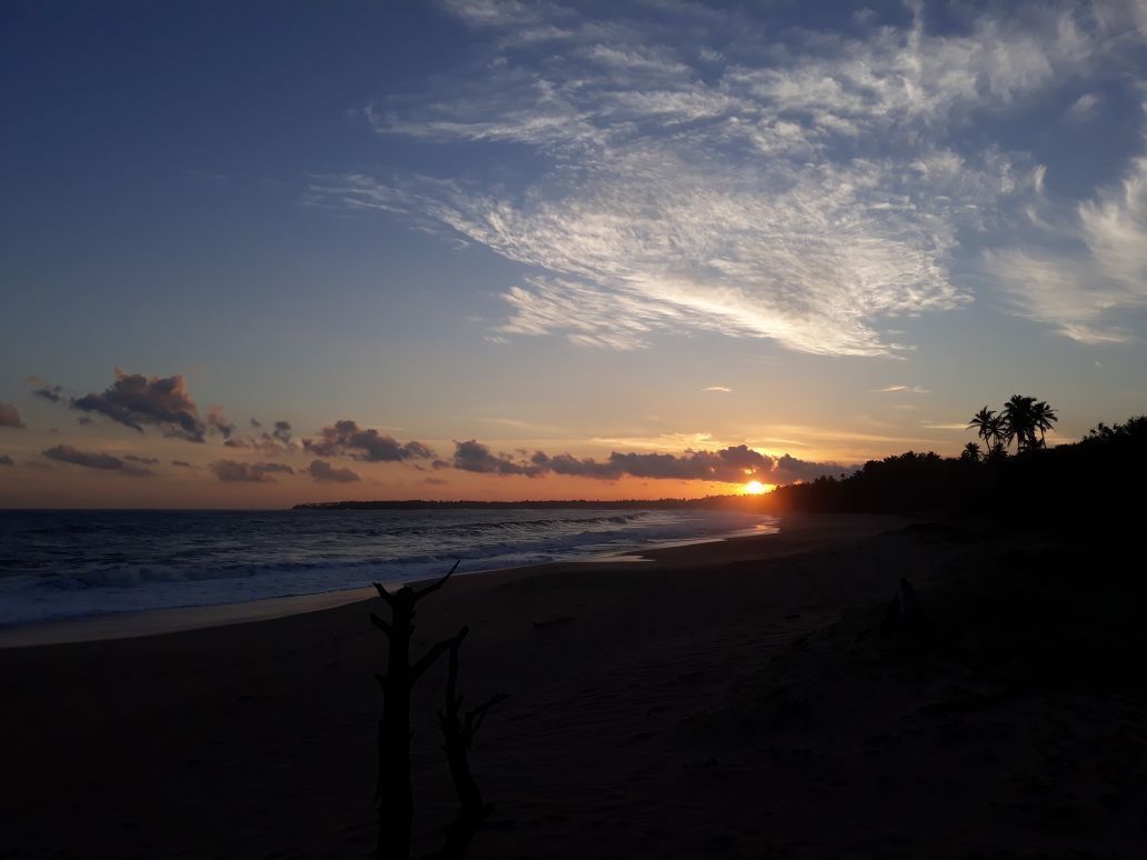 A beach at sunset with the sun setting over the ocean.