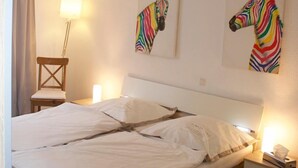Una cama bien tendida con sábanas blancas, cabecera de madera y dos cuadros con motivos de cebra.