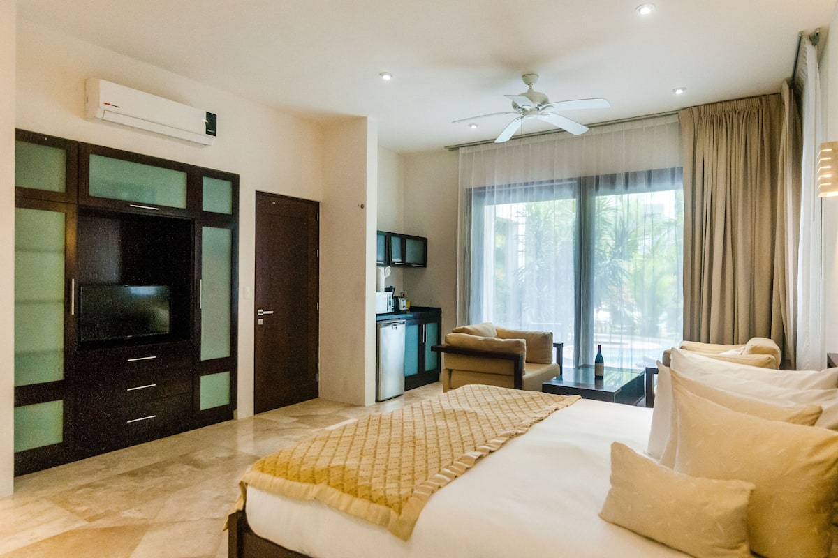 A hotel room with a bed, a TV, a desk, a chair, and a minibar.