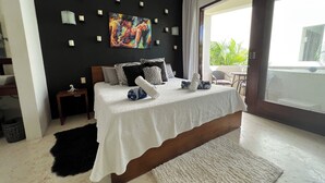 A modern bedroom with a large bed, a painting on the wall, and a view of greenery outside. - Mak Nuk Village Tulum II - Clothing Optional (Tulum)