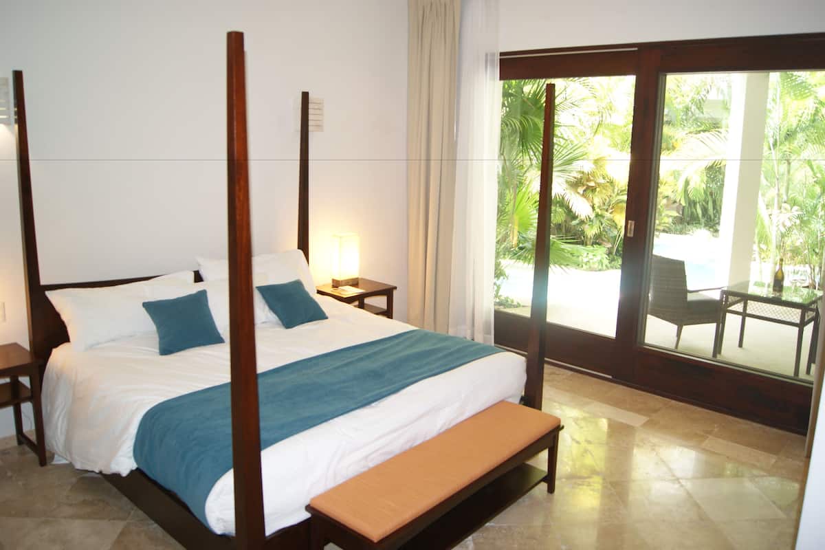 A four-poster bed with a bench, a nightstand, and a lamp.