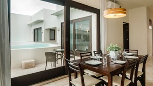 A dining area with a table set for four, a large window with a view of a pool and outdoor seating, and a modern pendant light. - Mak Nuk Village Tulum II - Clothing Optional (Tulum)
