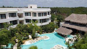A modern resort with a large swimming pool surrounded by lounge chairs and tropical vegetation. - Mak Nuk Village Tulum II - Clothing Optional (Tulum)