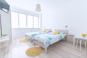 A bright bedroom with two beds, a small table, and a window with curtains. - The Dots Hostel (Zagreb)