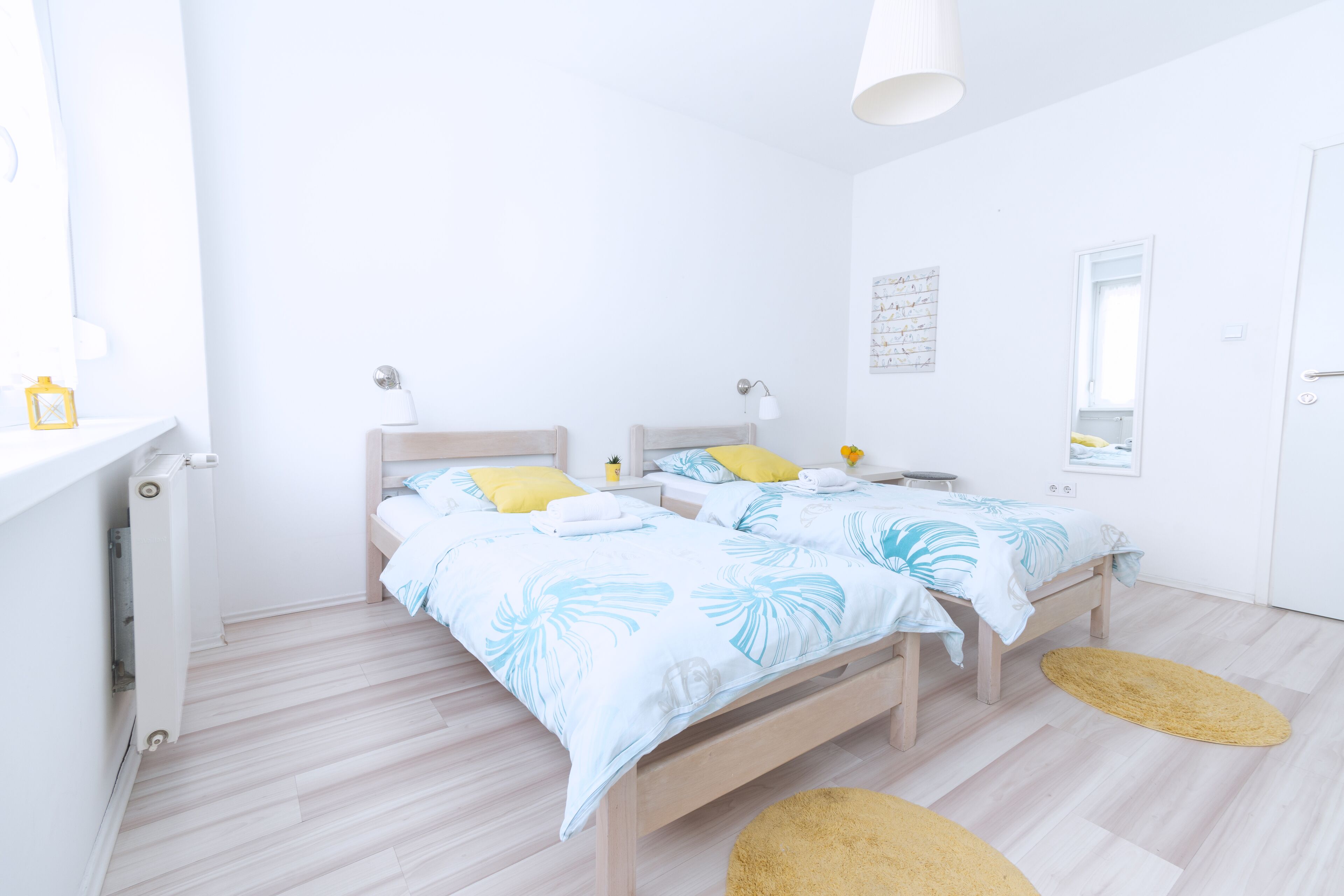 A modern bedroom with two beds, a white radiator, a small table, and a mirror on the wall.