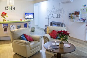 A hotel reception area with a reception desk, two sofas, a coffee table, and a wall with a cityscape mural. - The Dots Hostel (Zagreb)