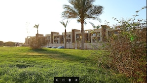 A residential area with modern buildings, a grassy lawn, and palm trees. - Alhayat Ain El Sokhna (Ataqah)