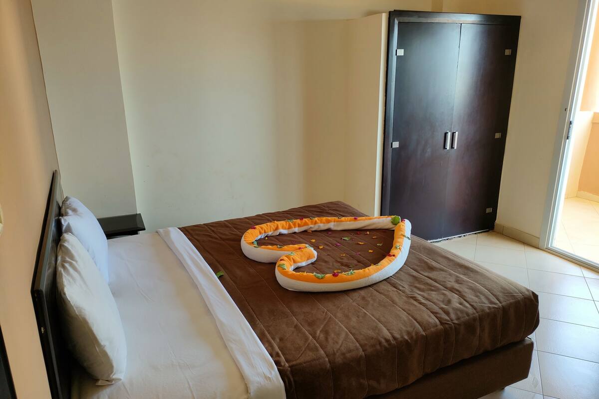 Ein Einzelbett mit brauner Bettdecke, einem weißen Kopfkissen und einem orange-weißen Haustierbettchen auf dem Bett.