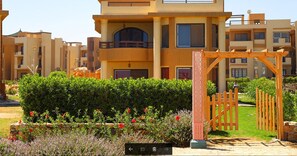 A multi-story residential building with balconies, a gated entrance, and well-maintained gardens.