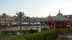 A gazebo in a landscaped area with a pool and umbrellas in the background. - Alhayat Ain El Sokhna (Ataqah)