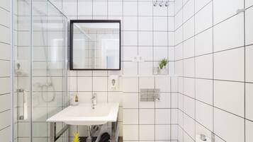 Un bany modern amb dutxa envidriada, un lavabo blanc i un mirall.