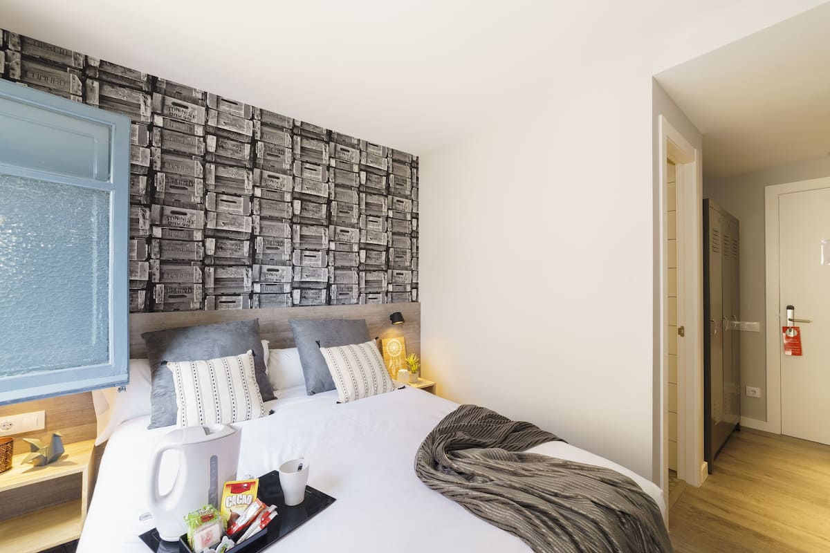 A hotel room with a bed, a nightstand, a wall with a patterned design, a door, and a hallway.