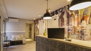 A modern hotel lobby with a reception desk, a laptop, a pineapple decoration, and a unique abstract wall mural. - BYPILLOW Wander (Barcelona)