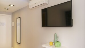 A hallway with a mounted TV, a white shelf with a cactus and a candle, and an air conditioning unit on the wall. - BYPILLOW Wander (Barcelona)