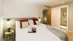 A modern hotel room with a brick-patterned headboard, a large bed with red and white pillows, a bedside table with a lamp, and an air conditioning unit on the wall. - BYPILLOW Wander (Barcelona)