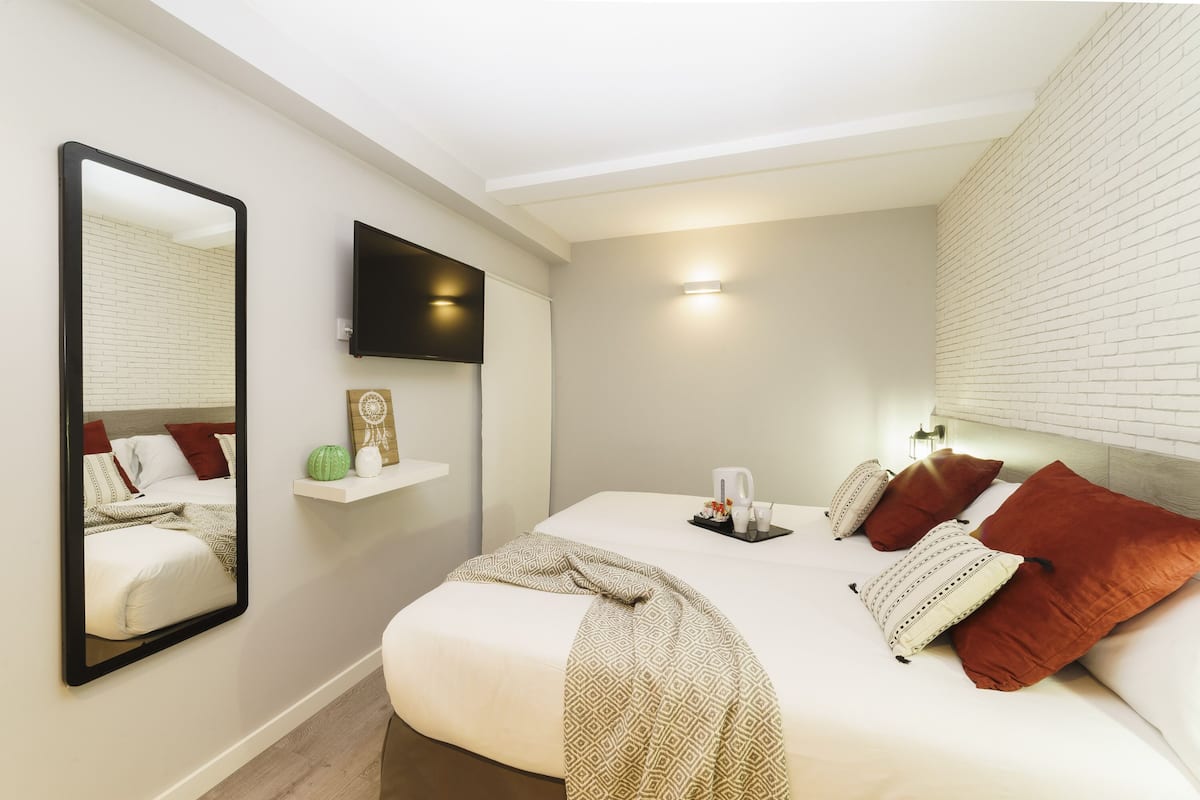 A modern bedroom with a large bed, a flat-screen TV, a bedside table with a lamp, and a wall-mounted shelf with decorative items.