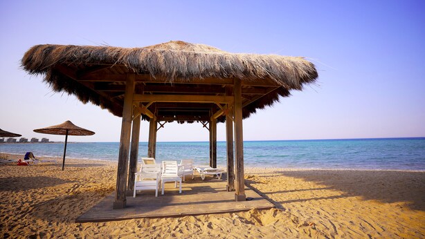 A beach hut with a thatched roof, white lounge chairs, and a wooden deck. - Blue Bay Asia Resort El Sokhna (Ataqah)