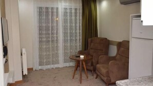 Una sala de estar con un sofá, una mesita redonda y una ventana con cortinas ligeras.