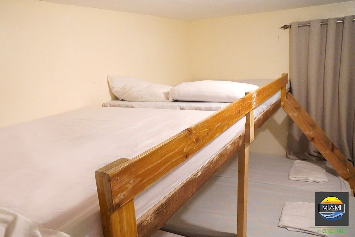 A single bed with a wooden frame in a room with plain walls and a curtain.