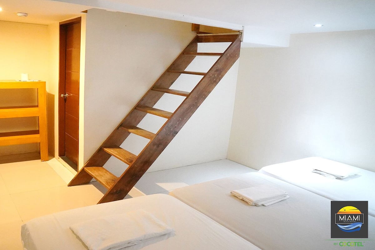 A bedroom with a wooden ladder staircase, a wooden wardrobe, and a bed with a folded towel.