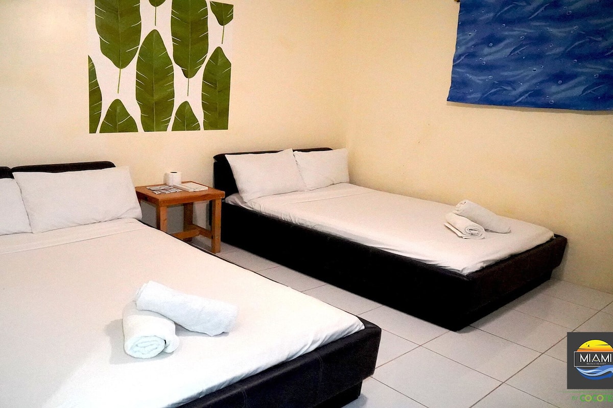 A hotel room with two beds, white linens, a small wooden nightstand, and a wall art piece.