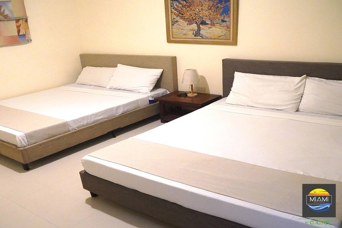 Two single beds with white linens, a nightstand with a lamp, and a painting on the wall.